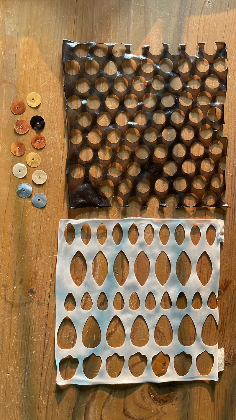 Punched material sheets and a row of coloured samples on a worktable